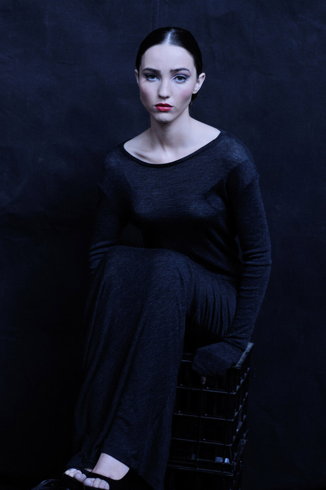 Sydney Fashion Photography - In Development, Model seated on a black milk create against a black canvas wearing a black knit dress. Maille - L/S Cowl Arm T-Shirt, Black BG Seated Editorial Fashion Photography
