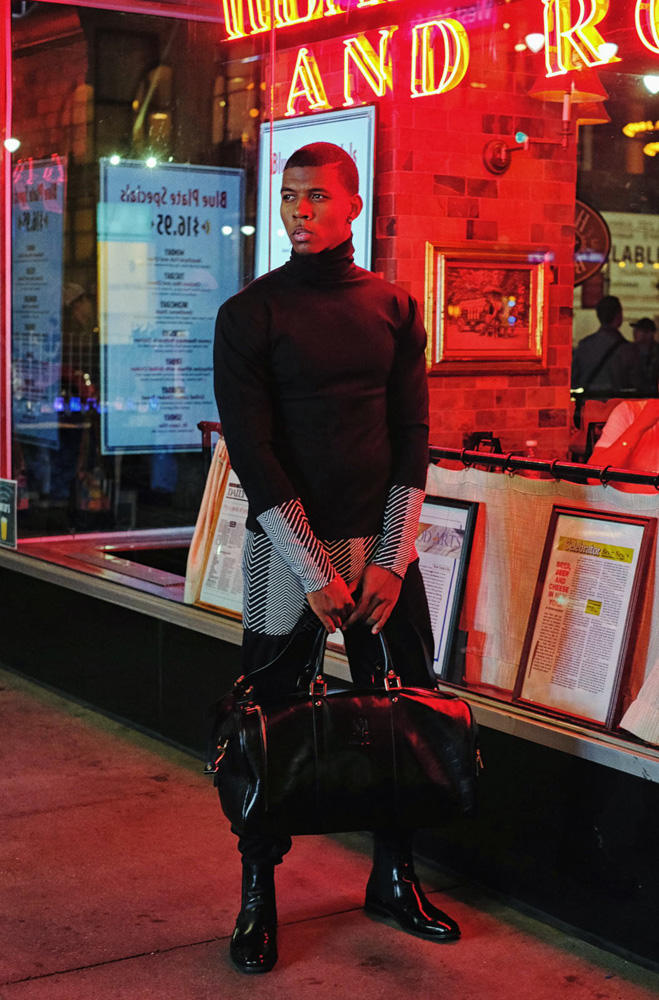 Asymmetrical turtle neck in a wash of red neon light at Empire State, full length with tote bag - Menswear photographed in New York City by Kent Johnson.