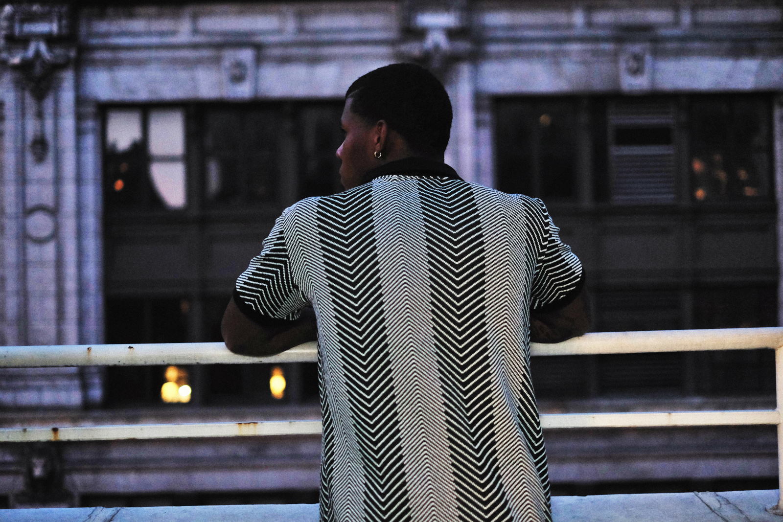 Collared herringbone vee neck tee shirt as seen from behind, twilight looking out at NYC. Menswear photographed in New York City by Kent Johnson.