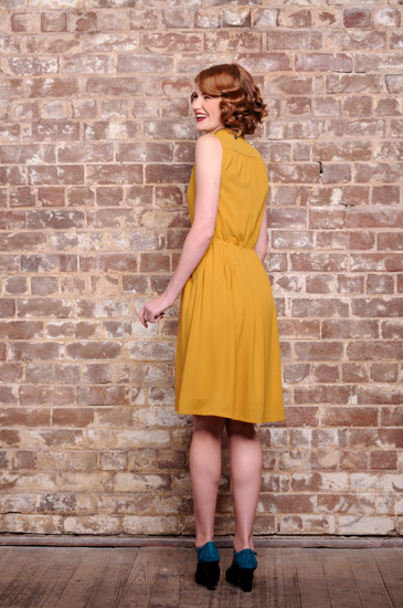 Model wears vintage inspired mustard colour dress shown from behind - Studio Fashion Photography by Kent Johnson.