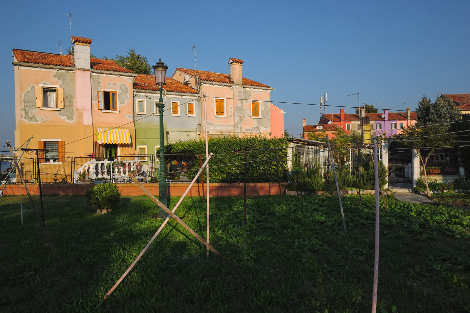 A backyard, rear view green grass, cloths line and colourful houses on Burano. Lifestyle photography by Kent Johnson.