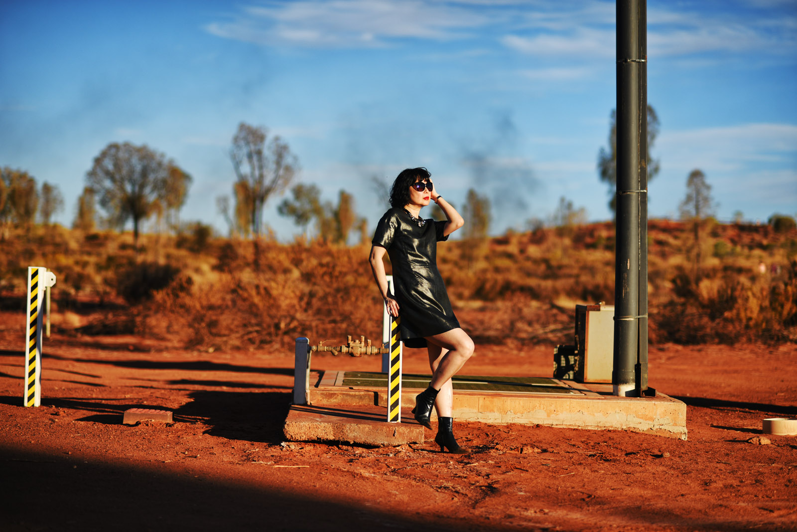 Red soil in the Central Australian outback Uluru, Vivienne in metalic dress at a small pumping station in the desert. Photoshoot by Kent Johnson for White Caviar Life.