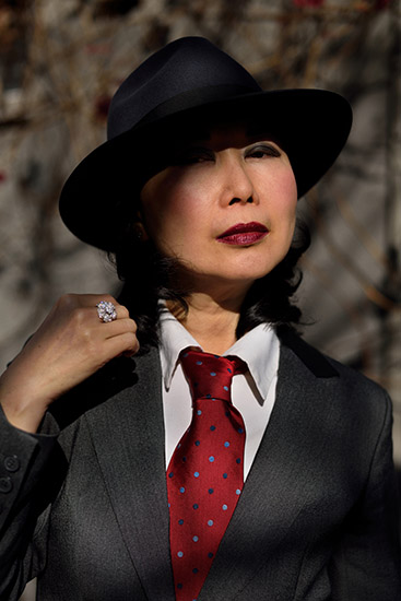 Fashionable lady gangster in Fedora, white shirt red tie and grey suit jacket.